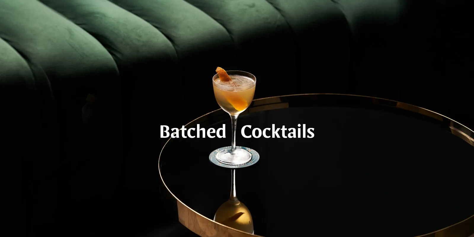 Cocktail Labels artwork: a coupe glass with citrus garnish on a brass table beside a dark green velvet banquette.